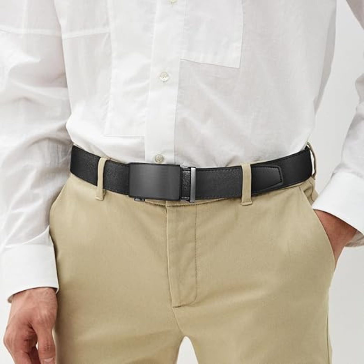 A lifestyle photo showing a men's leather ratchet belt in black being worn with khaki trousers and a white button-down shirt. The image demonstrates the belt's clean, professional fit and modern aesthetic for everyday wear.
