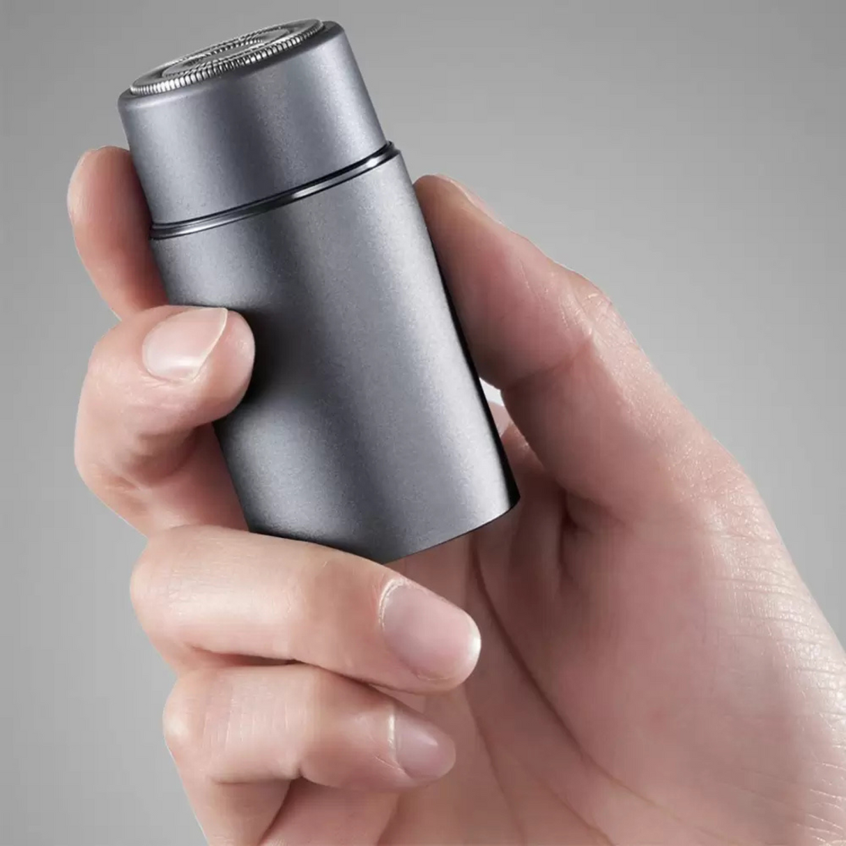 Hand holding a silver electric shaver against a gray background