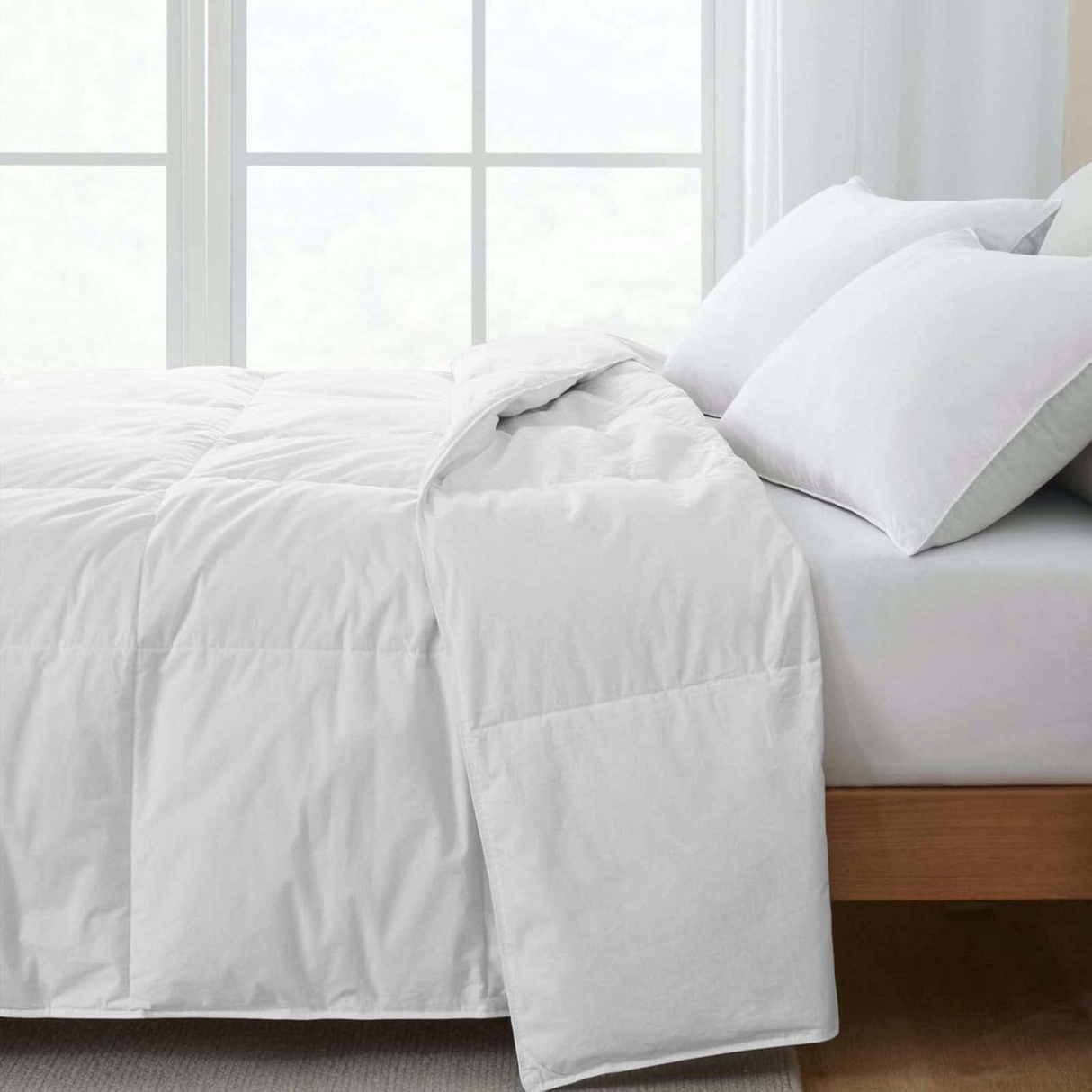 White duvet spread on bed with pillows in a bright bedroom setting.