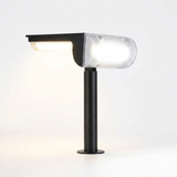A profile view of a black solar landscape light features a unique T-shaped head with illuminated front and side LED panels. The product is shown mounted on a short, sturdy post with a flat base, emphasizing its modern design and soft, warm light output.