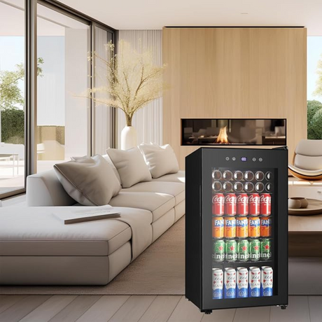 Compact drink refrigerator placed in a stylish living room next to a sofa and fireplace.