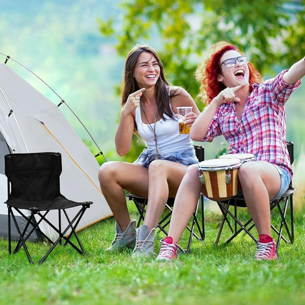 Two people enjoying outdoor camping while sitting on lightweight folding chairs near a tent.