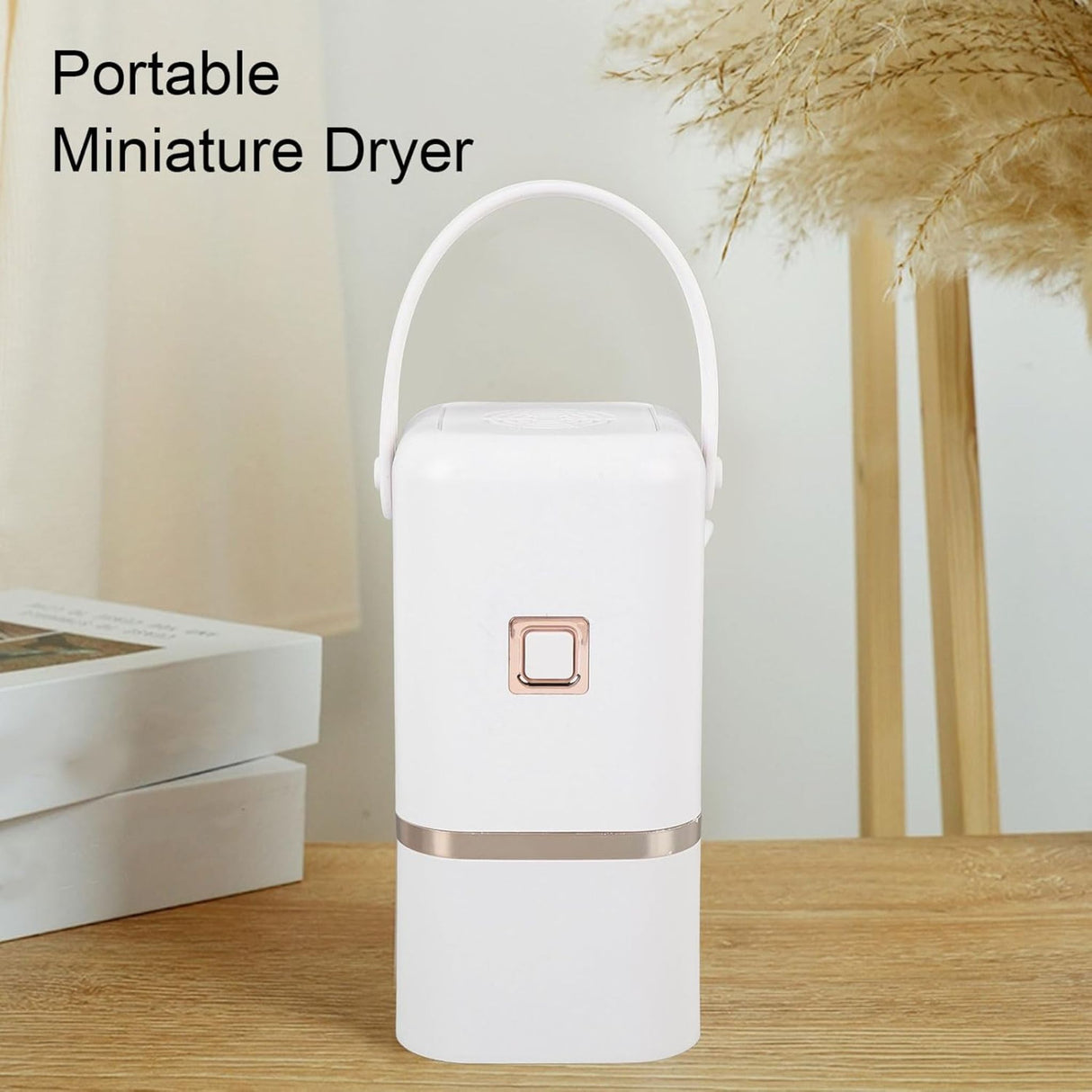 A white portable mini clothes dryer with a rose gold accent sitting on a wooden table in a brightly lit, minimalist room.