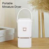 A white portable mini clothes dryer with a rose gold accent sitting on a wooden table in a brightly lit, minimalist room.