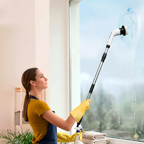 Woman using electric rotating cleaning brush with extension handle on window
