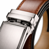 A close-up photo focusing on the high-quality brushed metal buckle of a men's leather ratchet belt. The sharp focus emphasizes the intricate mechanical details and the rich grain of the genuine leather.