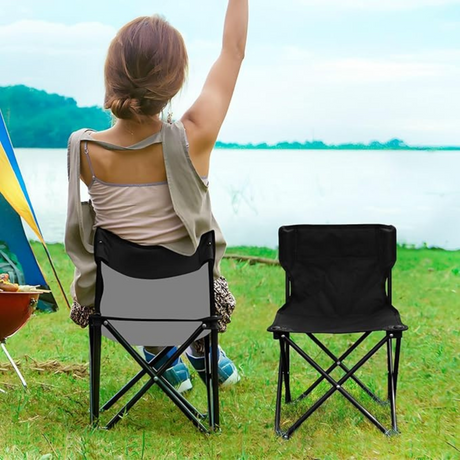 Person sitting on portable folding chair by a lakeside campsite with tent and outdoor setup.