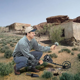 Person using a metal detector in a desert area, discovering an object buried in the ground.