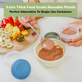 Person scooping baby puree into small container beside fresh fruits on a cutting board.