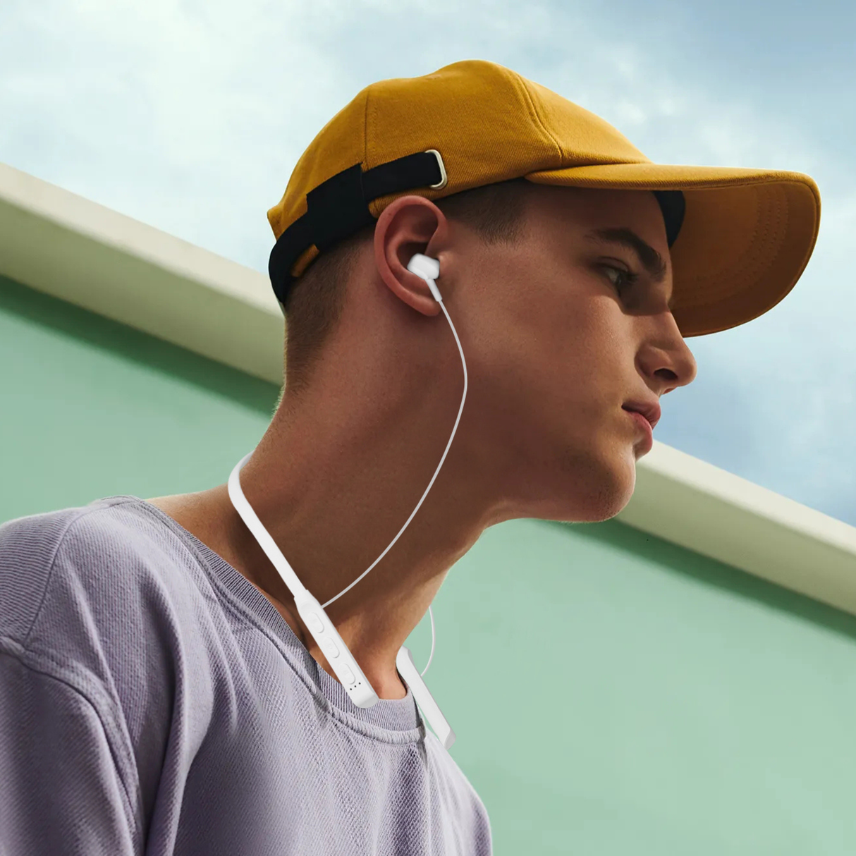 Man wearing neckband Bluetooth earphones outdoors while listening to music. Wireless earphones suitable for sports and active lifestyle.