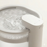 
A detailed close-up of a white cat water fountain highlighting its minimalist dispenser and clear rippling water. The soft lighting emphasizes the product's high-quality materials and clean design.